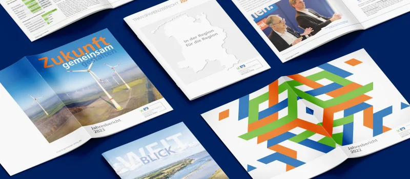 Mehrere geöffnete und geschlossene Jahres- und Transparenzberichte des Genossenschaftsverbands Weser-Ems liegen auf blauem Untergrund. Das Bild steht für Einblicke in Entwicklungen, Kennzahlen und Aktivitäten des Verbands.