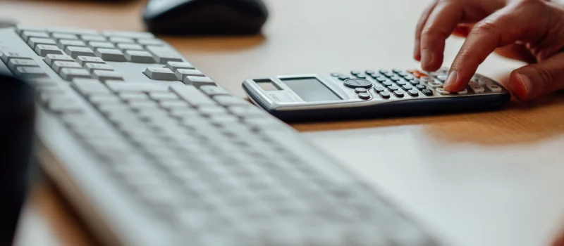 Eine Hand bedient einen Taschenrechner neben einer Computertastatur auf einem Schreibtisch. Das Bild steht für Kennzahlen, Struktur und Zusammenarbeit innerhalb der Genossenschaftlichen FinanzGruppe.