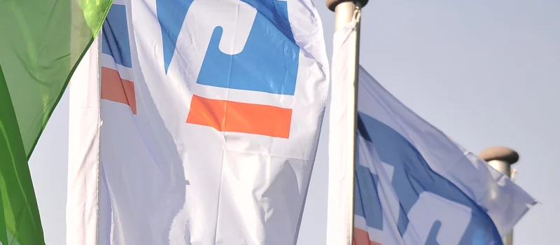 Weiße VR-Flaggen und eine grüne Raiffeisen-Flagge wehen vor hellem Himmel. Das Bild steht für die Volksbanken und Raiffeisenbanken als genossenschaftliche Banken in Weser-Ems.