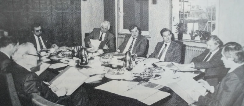 Historische Schwarz-Weiß-Aufnahme einer Besprechung mit mehreren Personen an einem Tisch. Das Bild begleitet den Meilenstein zum Ausbau der Raiffeisen-Werbegemeinschaft Weser-Ems im Jahr 1984.