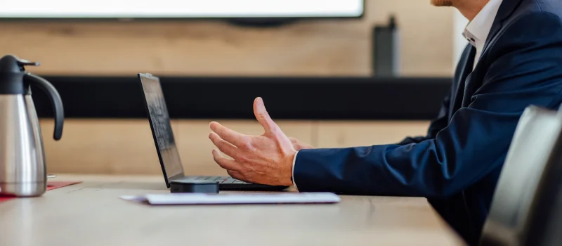 Ein Berater sitzt in einem Besprechungsraum an einem Laptop und gestikuliert im Gespräch. Das Bild steht für KundenFokus und die vertriebliche Weiterentwicklung von Genossenschaftsbanken.