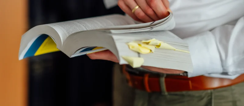 Eine Person blättert in einem mit Haftnotizen markierten Fachbuch. Das Bild steht für sorgfältige rechtliche Prüfung und Rechtsberatung beim Genossenschaftsverband Weser-Ems.