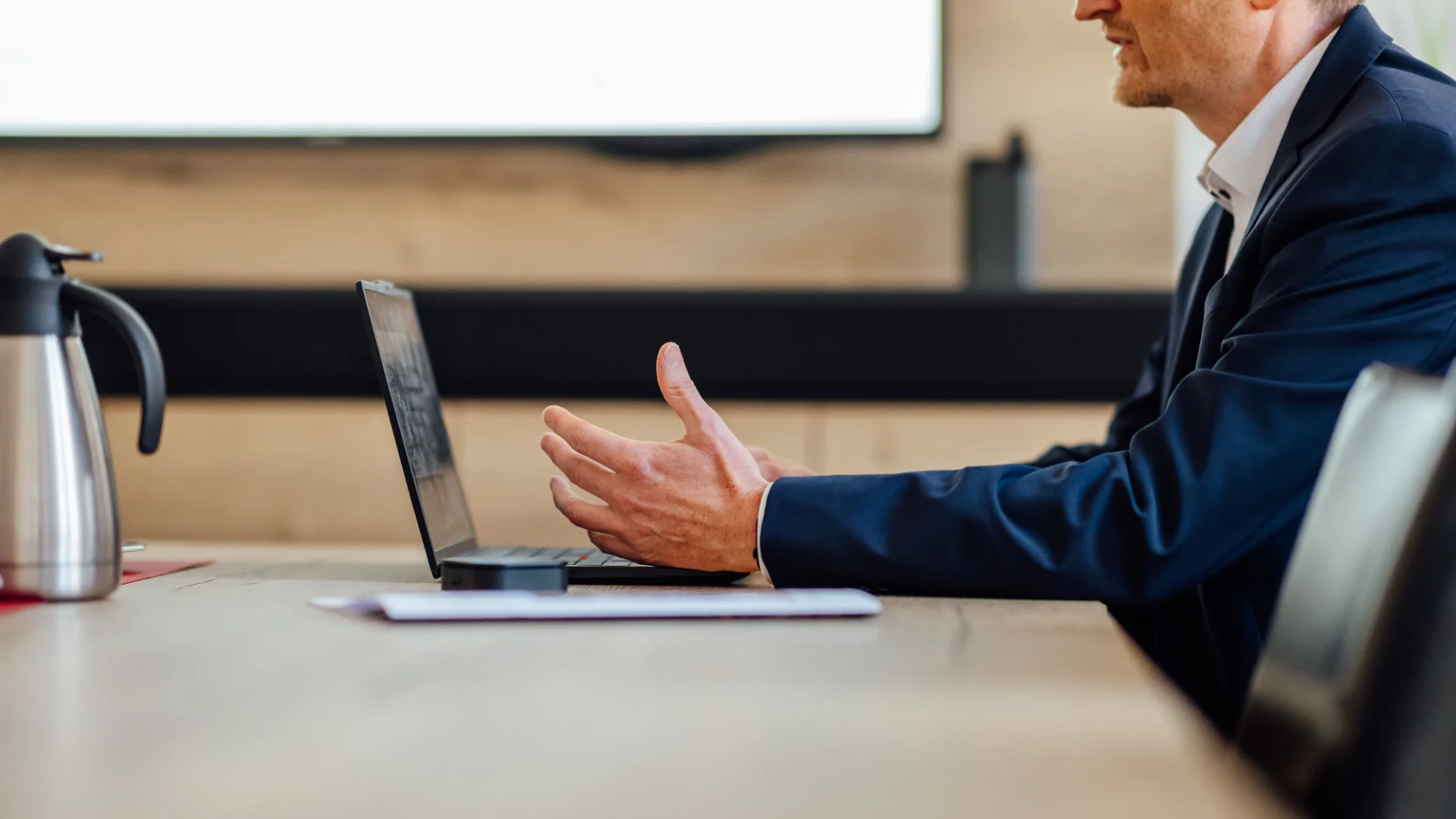 Ein Berater sitzt in einem Besprechungsraum an einem Laptop und gestikuliert im Gespräch. Das Bild steht für KundenFokus und die vertriebliche Weiterentwicklung von Genossenschaftsbanken.