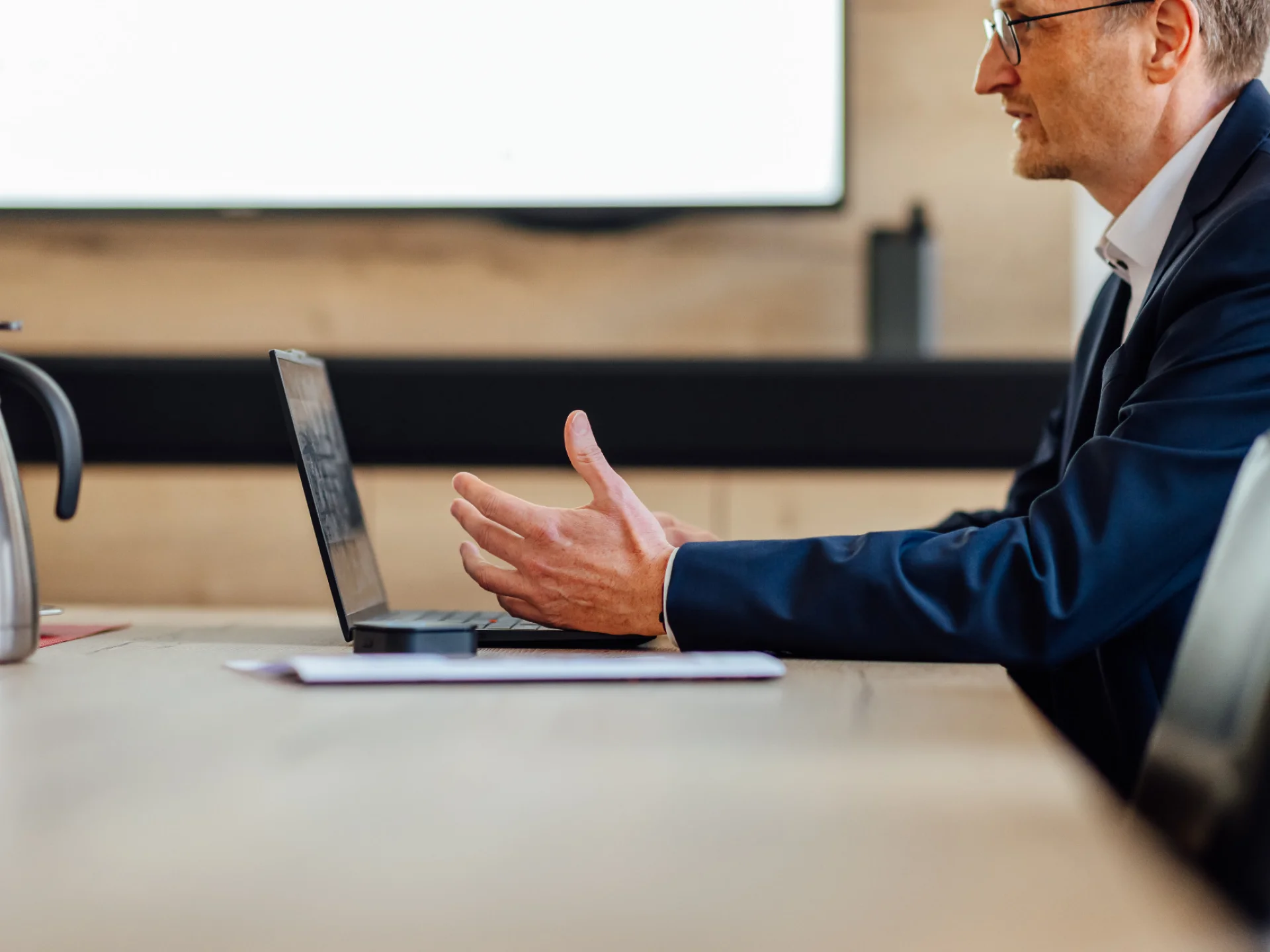 Ein Berater sitzt in einem Besprechungsraum an einem Laptop und gestikuliert im Gespräch. Das Bild steht für KundenFokus und die vertriebliche Weiterentwicklung von Genossenschaftsbanken.