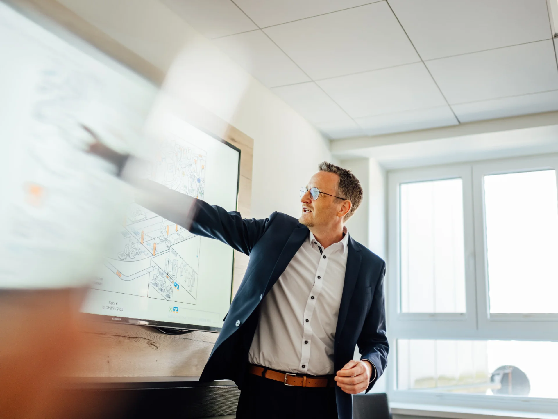 Ein Mann in Geschäftskleidung zeigt in einem Besprechungsraum auf eine digitale Darstellung. Das Bild steht für die strategische Nachhaltigkeitsberatung von Genossenschaftsbanken.