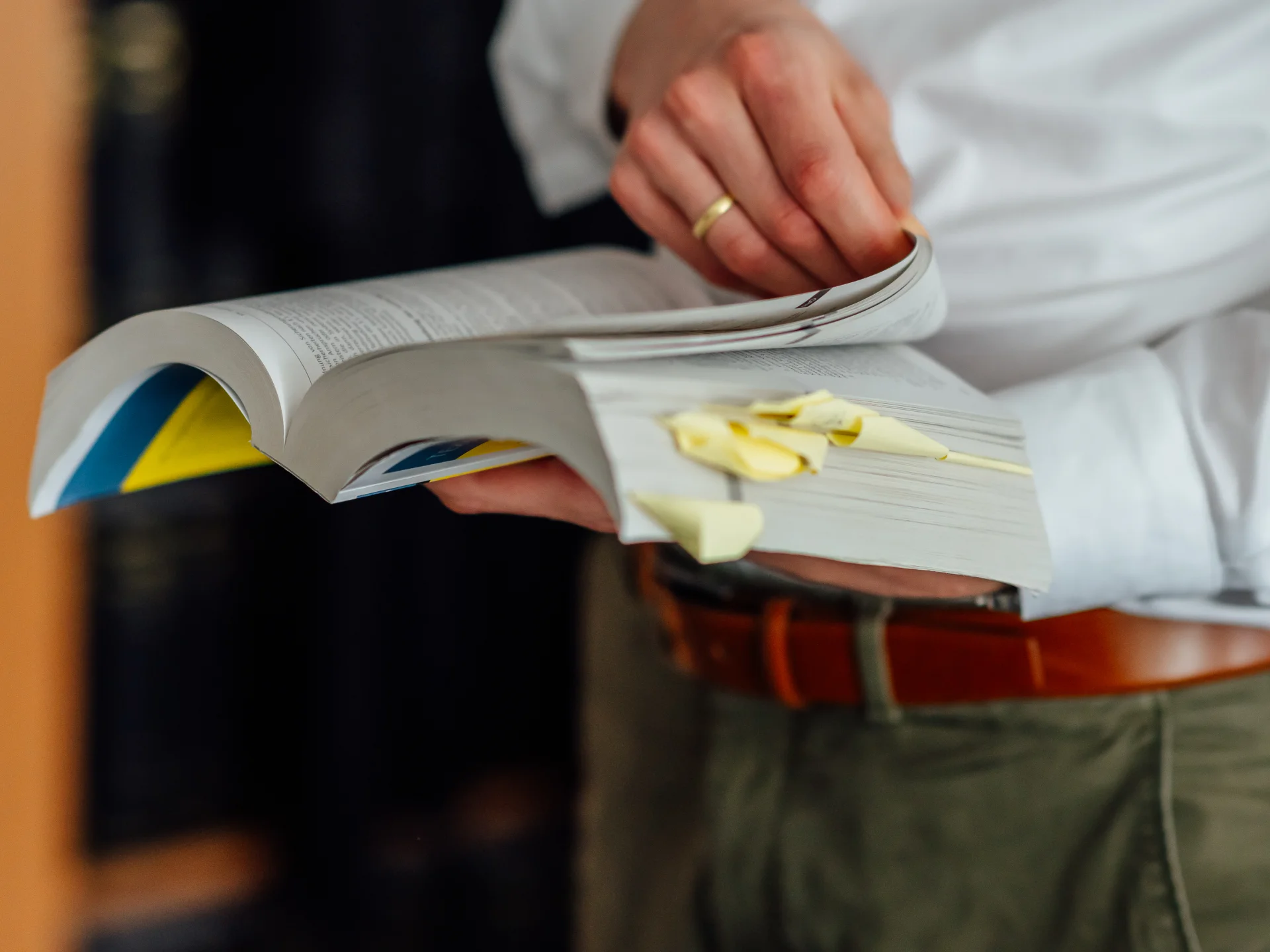Eine Person blättert in einem mit Haftnotizen markierten Fachbuch. Das Bild steht für sorgfältige rechtliche Prüfung und Rechtsberatung beim Genossenschaftsverband Weser-Ems.