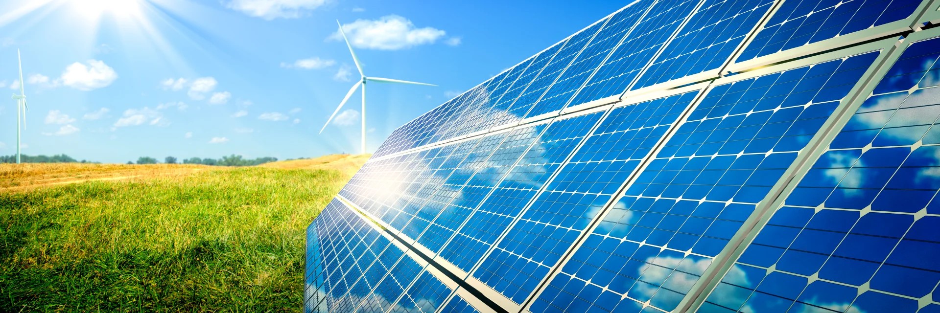 Solarmodule stehen auf einer Wiese, im Hintergrund sind Windenergieanlagen zu sehen. Das Bild steht für erneuerbare Energie aus Wind und Sonne und die Arbeit der Energiegenossenschaften in Weser-Ems.