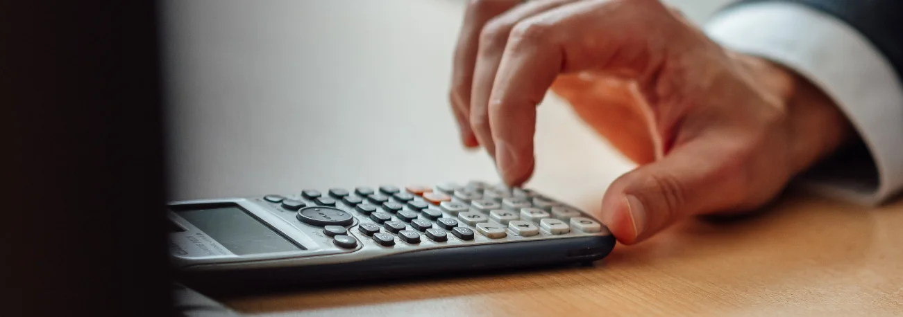 Eine Hand bedient einen Taschenrechner auf einem Schreibtisch. Das Bild steht für finanzielle Auswertung, spezialisierte Dienstleistungen und die Zusammenarbeit in der Genossenschaftlichen FinanzGruppe.
