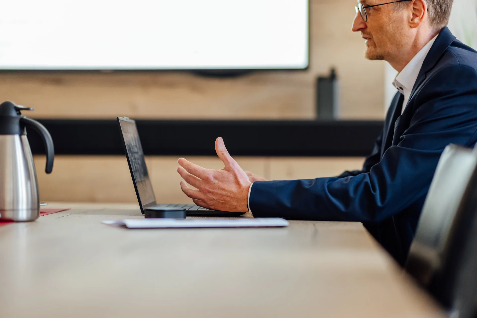 Ein Berater sitzt in einem Besprechungsraum an einem Laptop und gestikuliert im Gespräch. Das Bild steht für KundenFokus und die vertriebliche Weiterentwicklung von Genossenschaftsbanken.