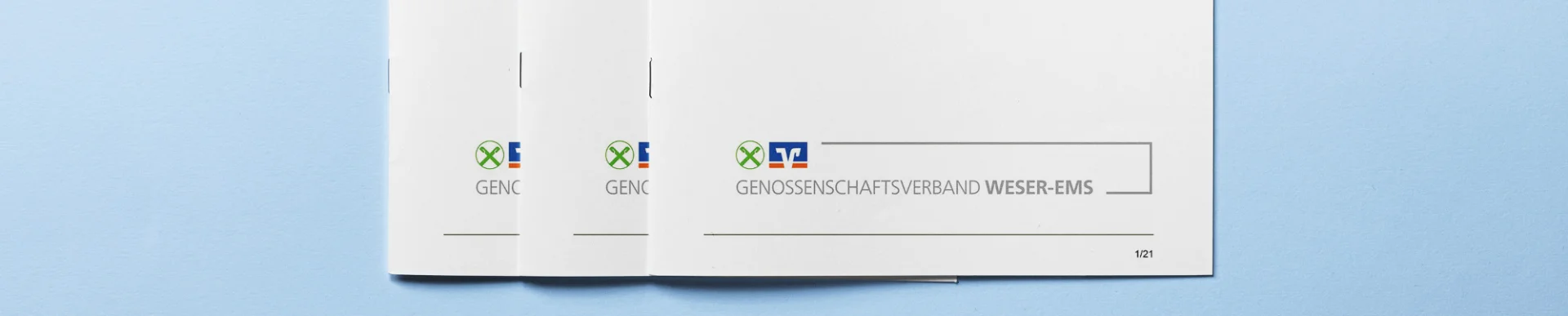 Mehrere Exemplare der Satzung des Genossenschaftsverbands Weser-Ems liegen auf hellblauem Untergrund.