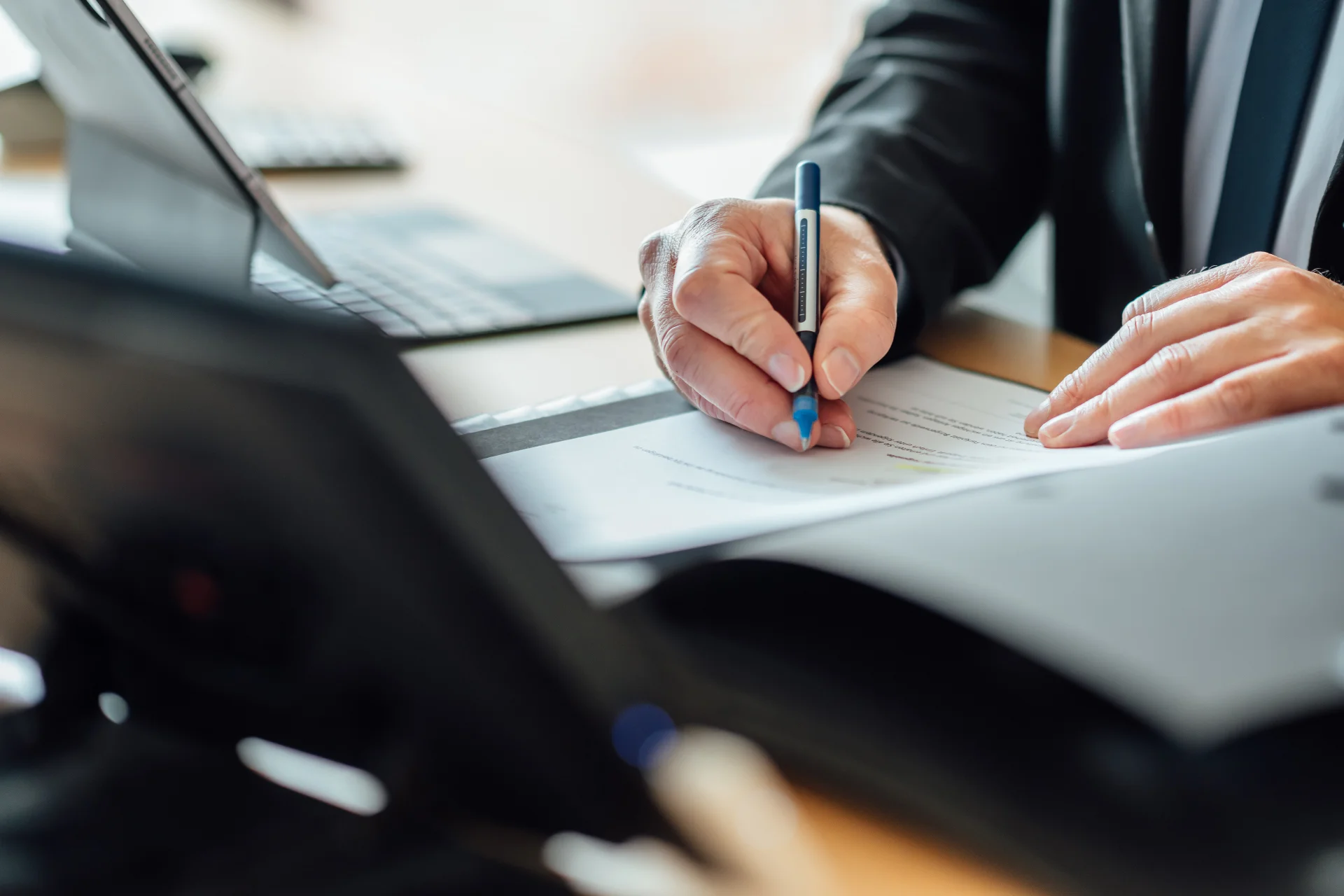 Eine Person markiert mit einem Stift eine Stelle in einem Dokument; daneben liegen Laptop und weitere Unterlagen. Das Bild steht für sorgfältige Steuerberatung und steuerliche Orientierung beim Genossenschaftsverband Weser-Ems.