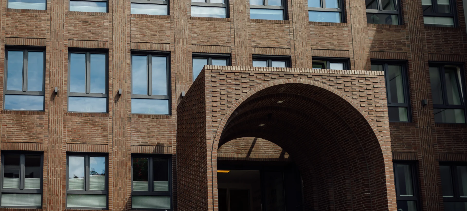 Fassade und Eingang zum Sitz des Genossenschaftsverbands Weser-Ems mit Backsteinbogen und Fensterfront.